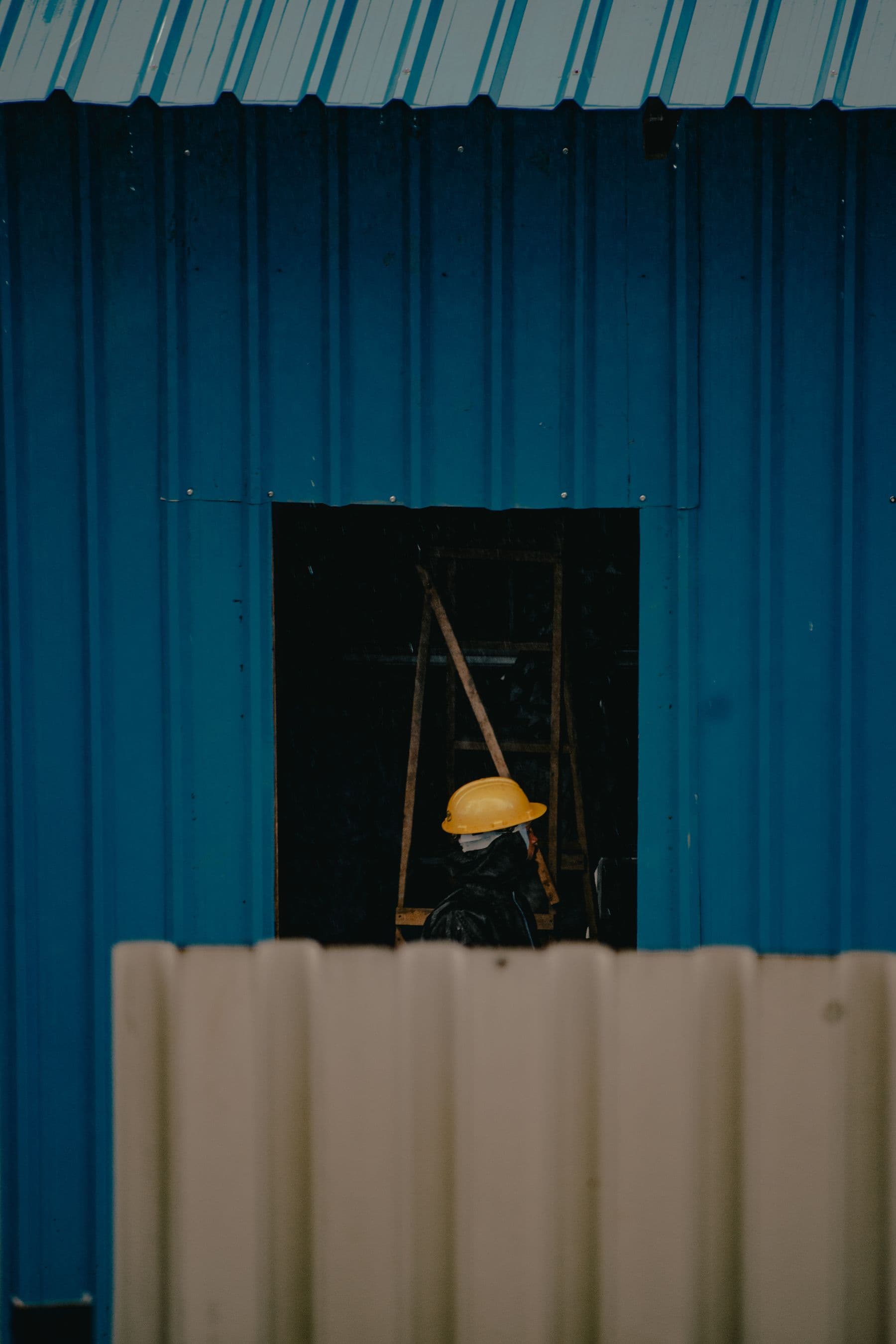 Person mit Schutzhelm hinter einer Bauabsperrung