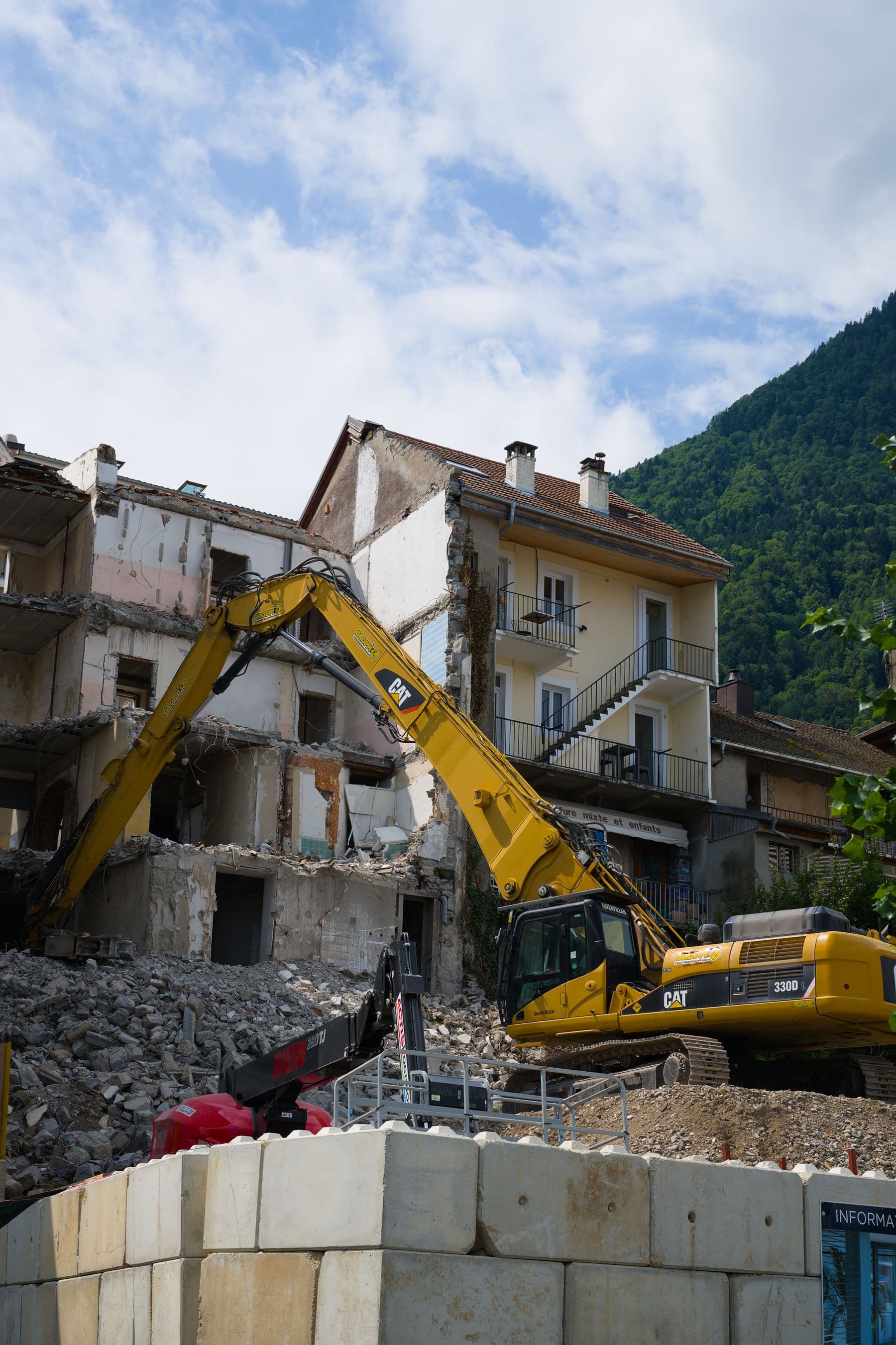 Bagger bricht ein Gebäude neben der stehen bleibenden Bebauung ab